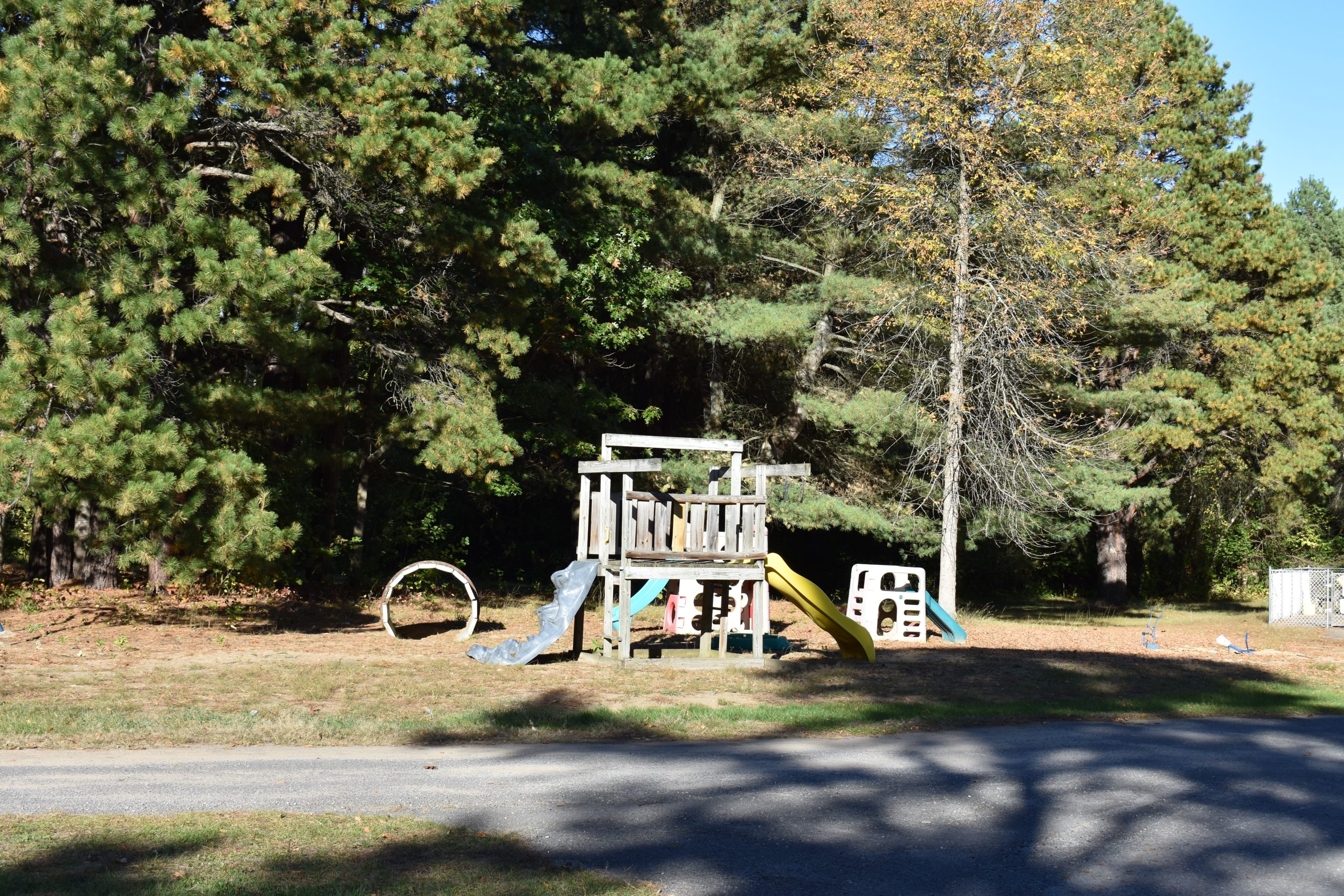 Wooden playground with slides, tire swing, and climbing platform surrounded by tall pine trees at a campground in Peru, NY