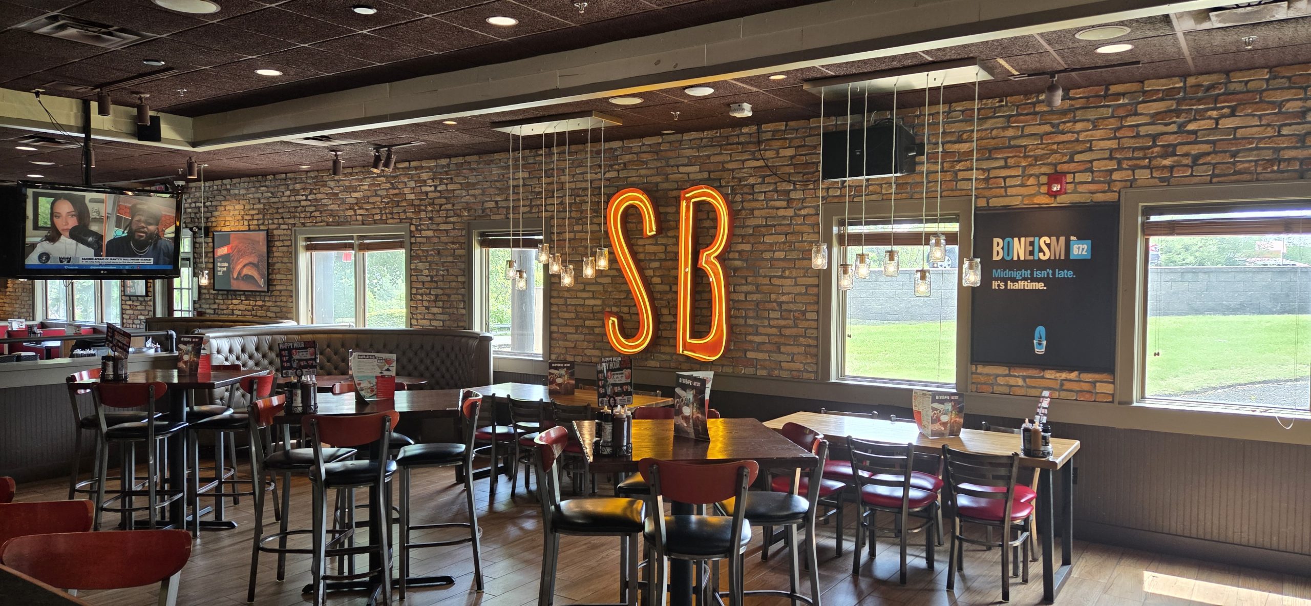 Interior of an on-site restaurant and bar with neon SB sign, brick walls, high-top tables, and pendant lighting near a campground in Massachusetts