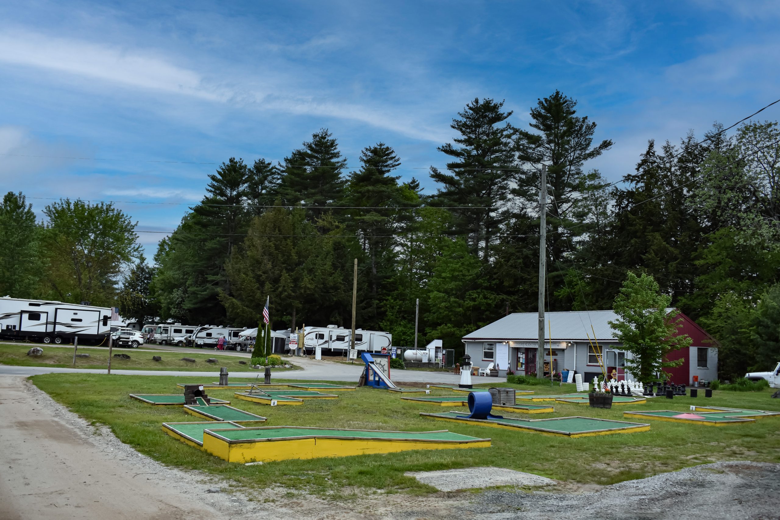 Mini golf course with colorful putting greens near RV sites and campground buildings surrounded by tall pine trees at a campground near Mount Sunapee