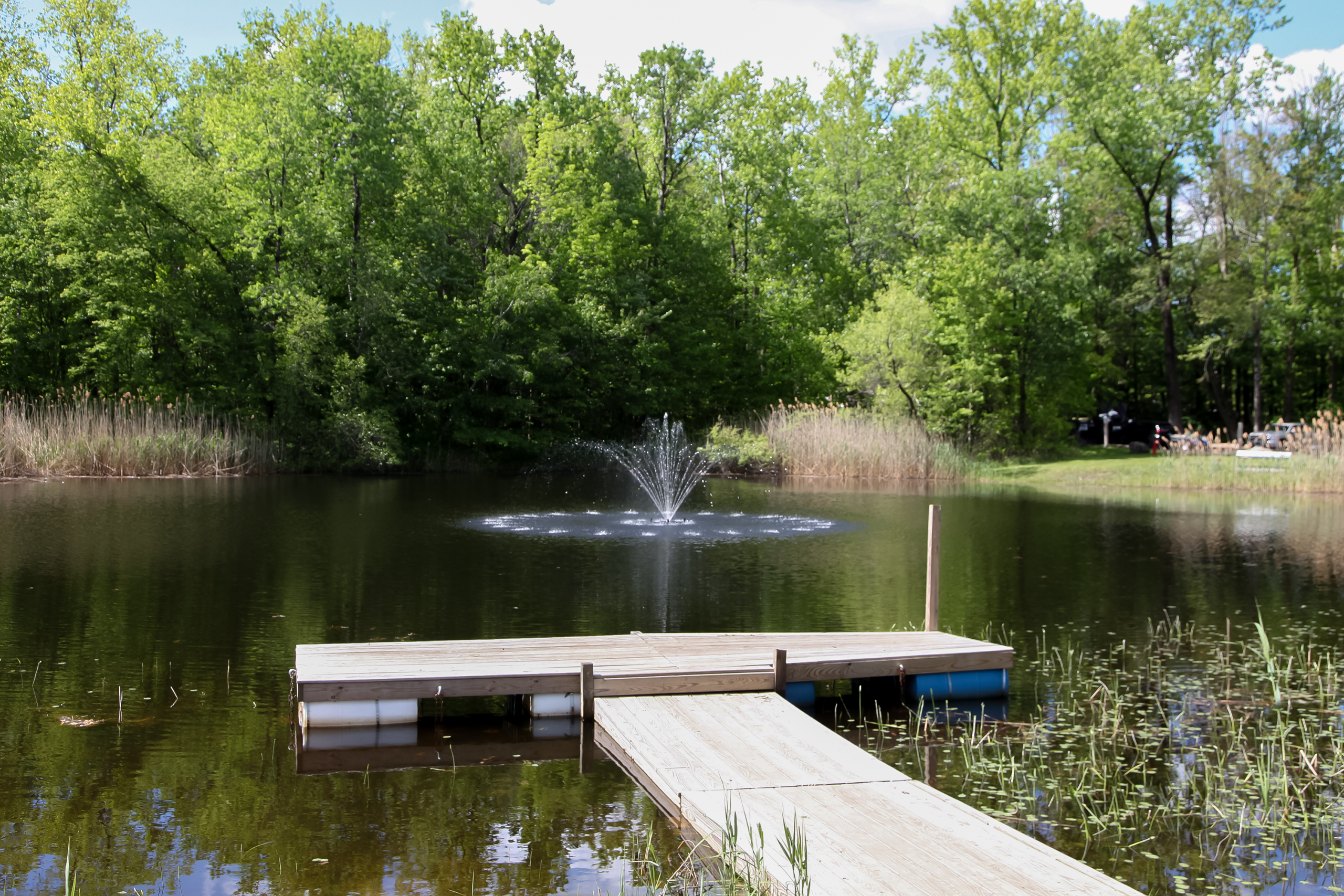 Wooden floating dock on a serene pond with a water fountain and lush green trees at a campground in Barkhamsted, CT