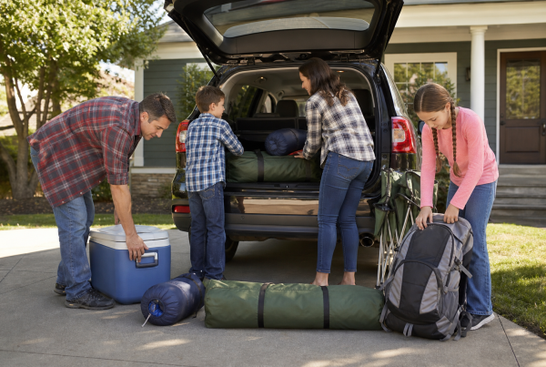 Family packing their SUV with camping gear including a tent, cooler, sleeping bags, and backpack.