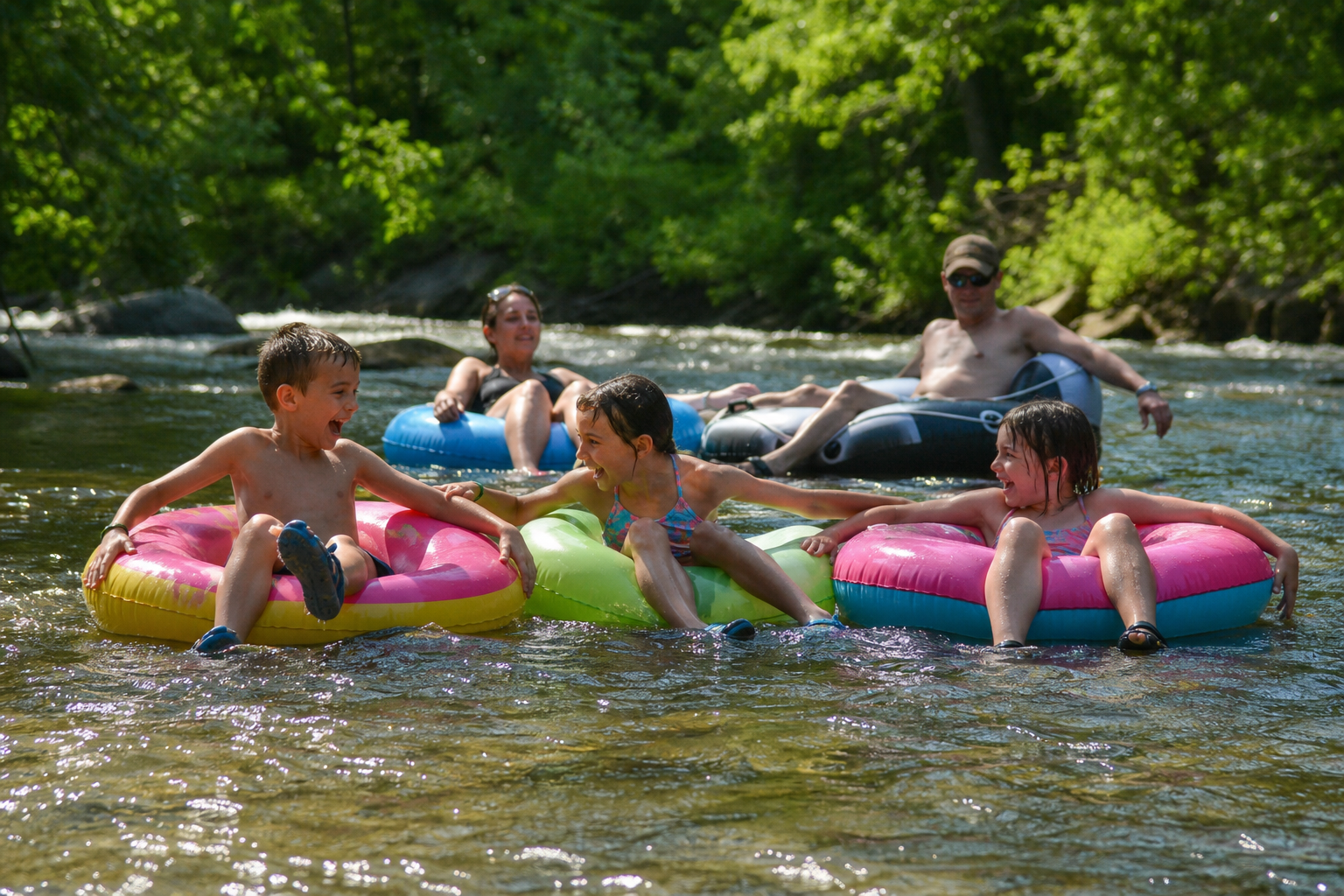 Family tubing down a gentle river on colorful inner tubes on a sunny day.