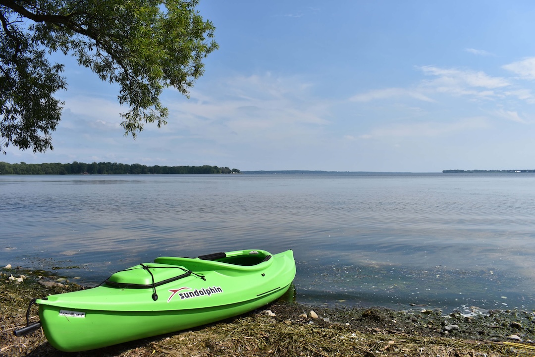Bright green kayak resting on the shore of Lake Champlain under a clear summer sky.