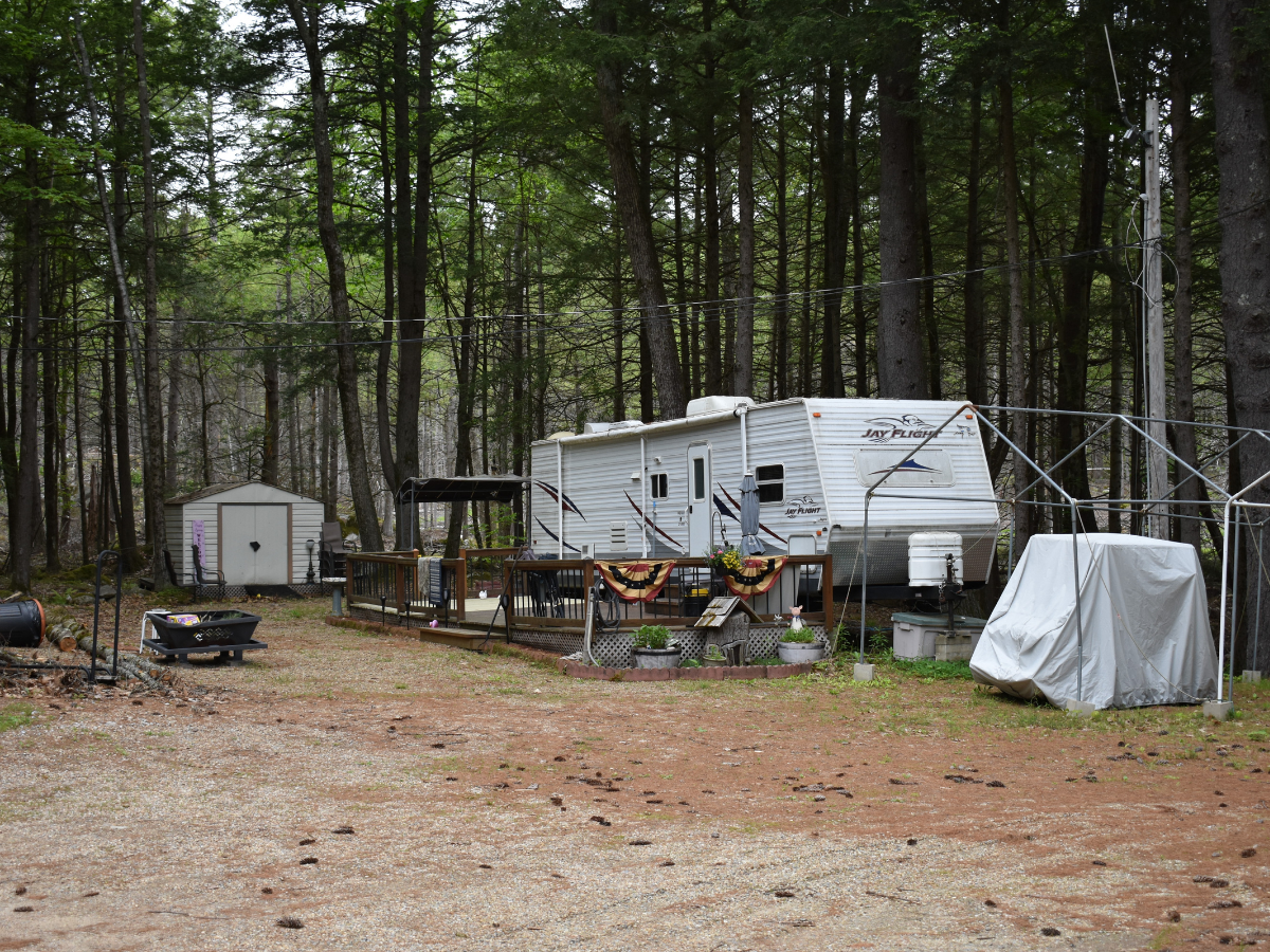 Travel trailer with a wooden deck, picnic table and fire pit at a wooded campsite.